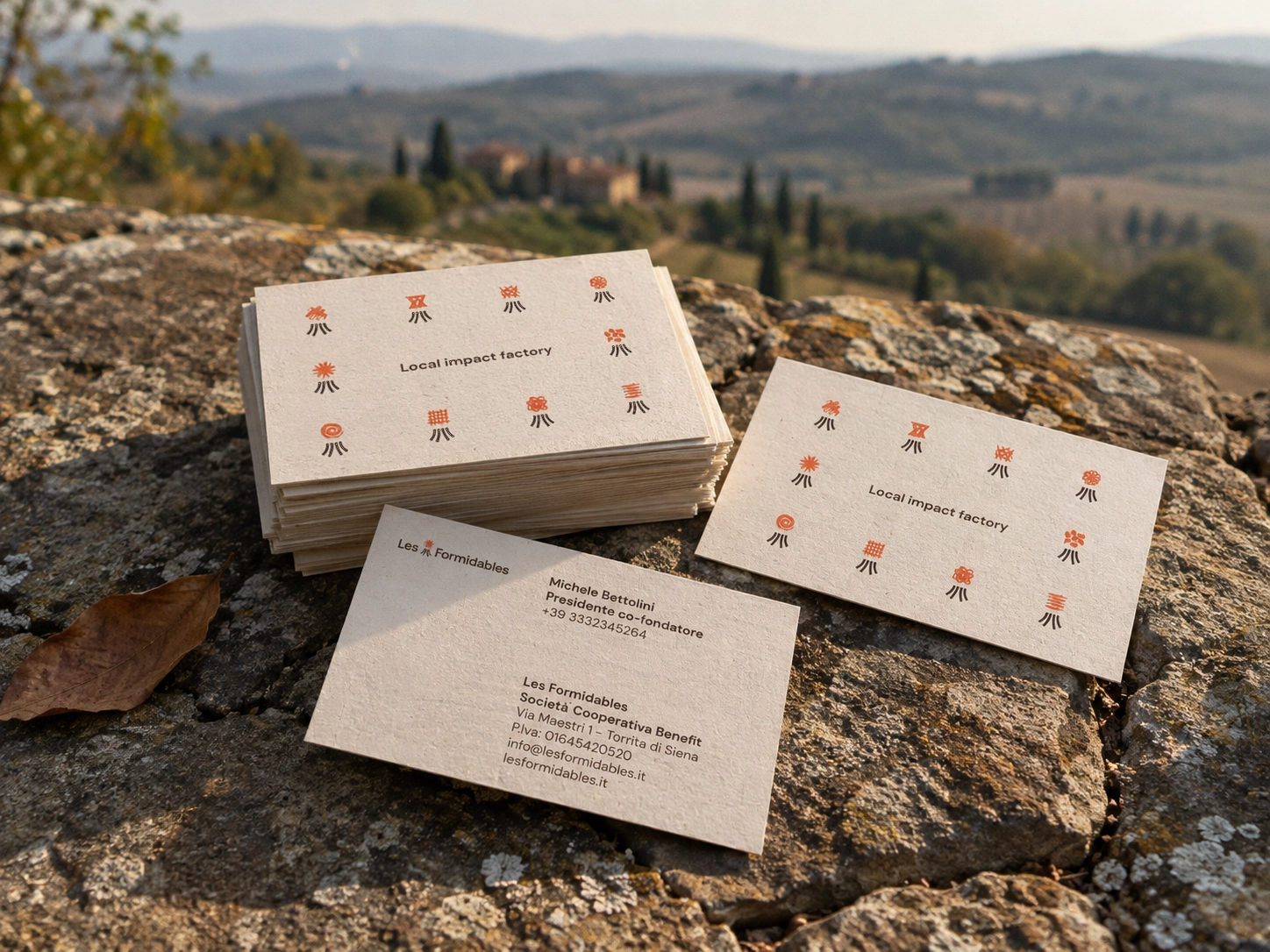 Biglietti da visita Les Formidables con le varianti del simbolo, appoggiati su una roccia nel paesaggio toscano